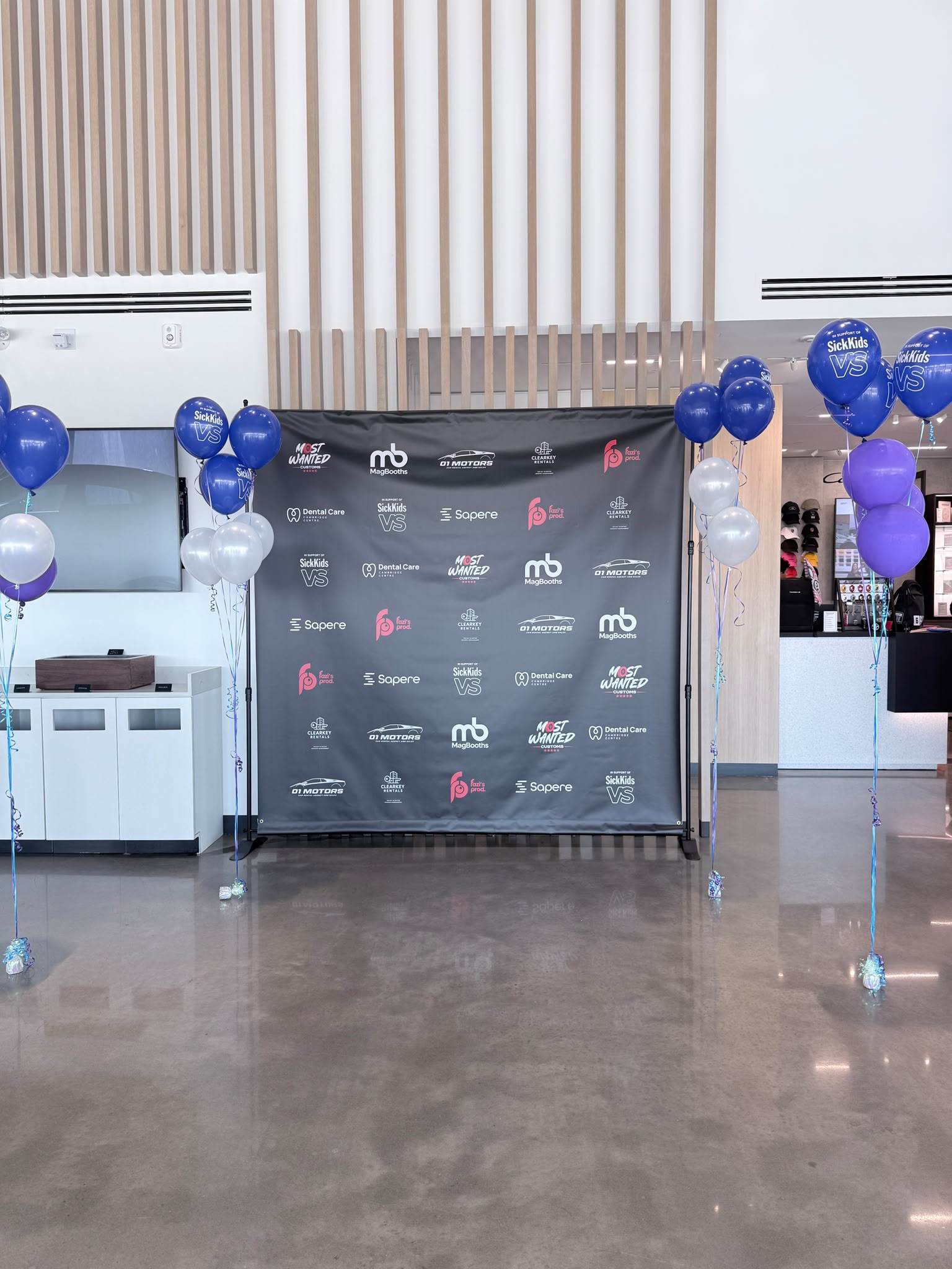 Sapere sponsor backdrop at the SickKids VS Charity Car Show, Porsche Experience Centre Toronto, with blue and purple SickKids balloons flanking the step-and-repeat